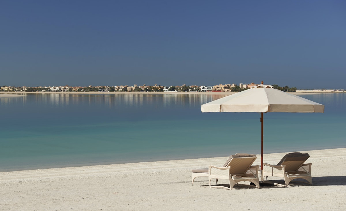 Two lounge chairs under an umbrella on a sandy beach