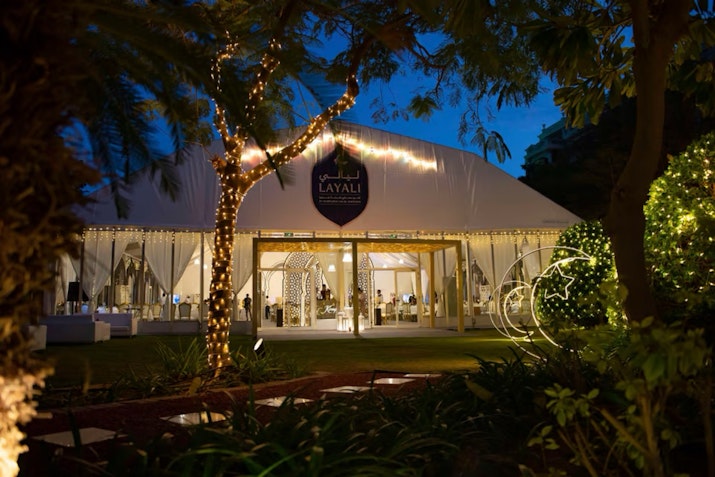Illuminated outdoor event tent at night, surrounded by trees and string lights