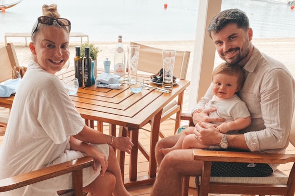A family enjoying time together at a table near the beach, with a baby in the father's lap.