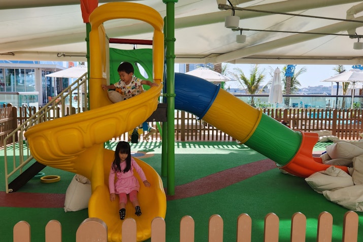 Two children playing on a colorful slide and climbing structure in a playground.