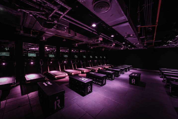 A dimly lit, club-style workout studio with benches and workout equipment.