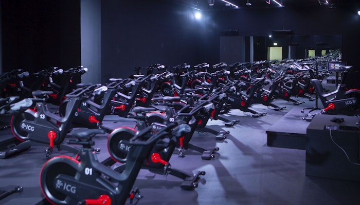 700 Padel & Fitness Hub An indoor cycling studio filled with rows of stationary bikes under vibrant lighting.
