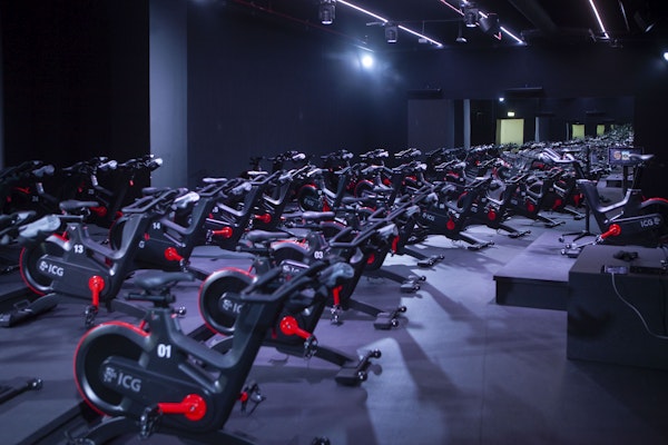 An indoor cycling studio filled with rows of stationary bikes under vibrant lighting.