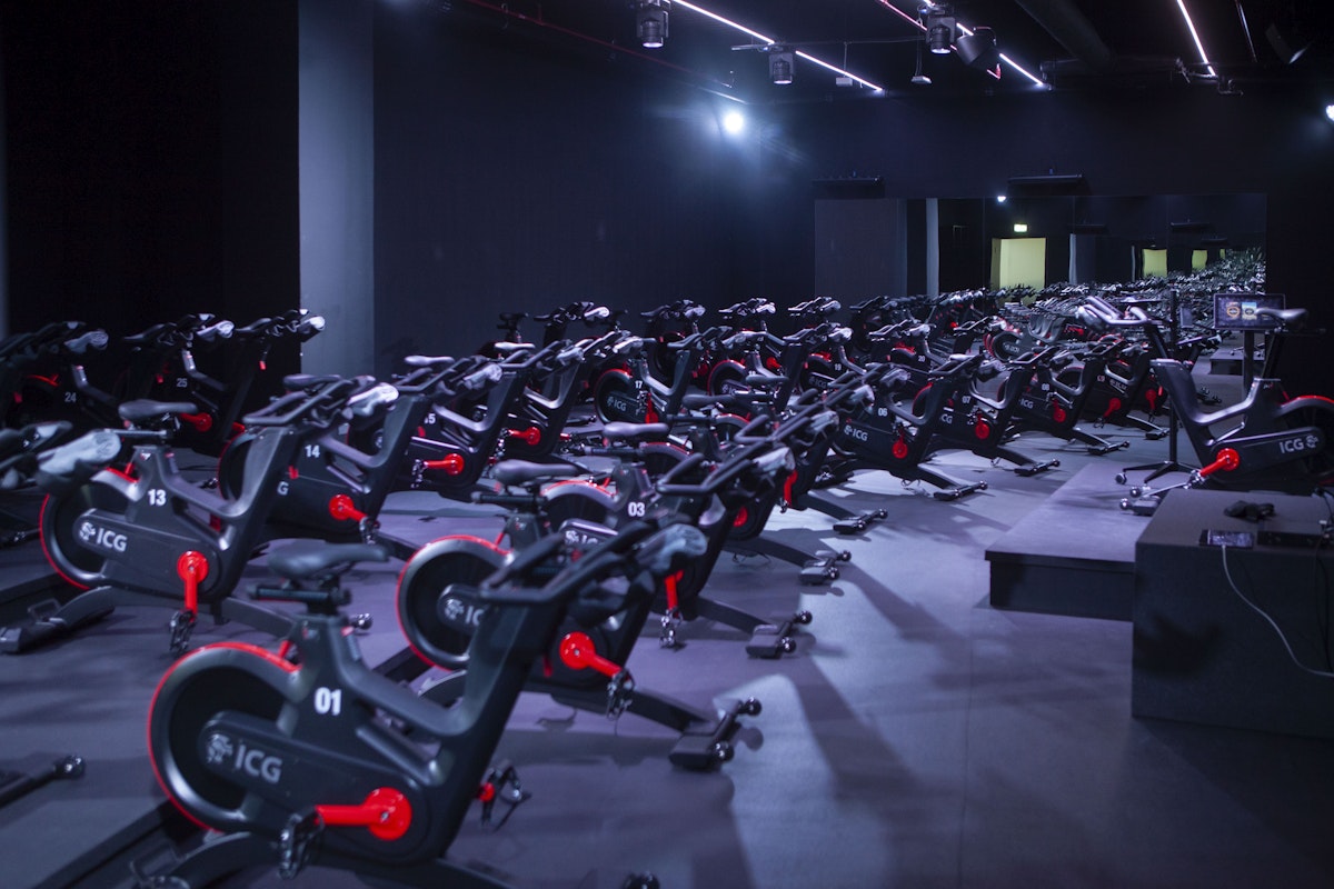An indoor cycling studio filled with rows of stationary bikes under vibrant lighting.
