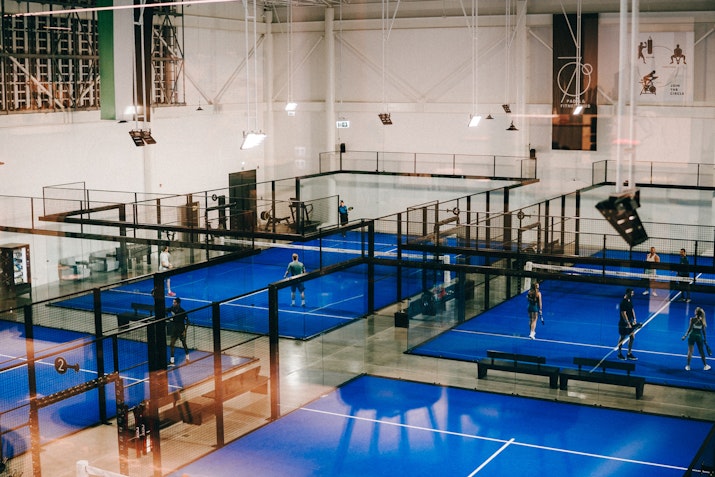 Indoor sports facility featuring multiple blue courts and players engaged in activities