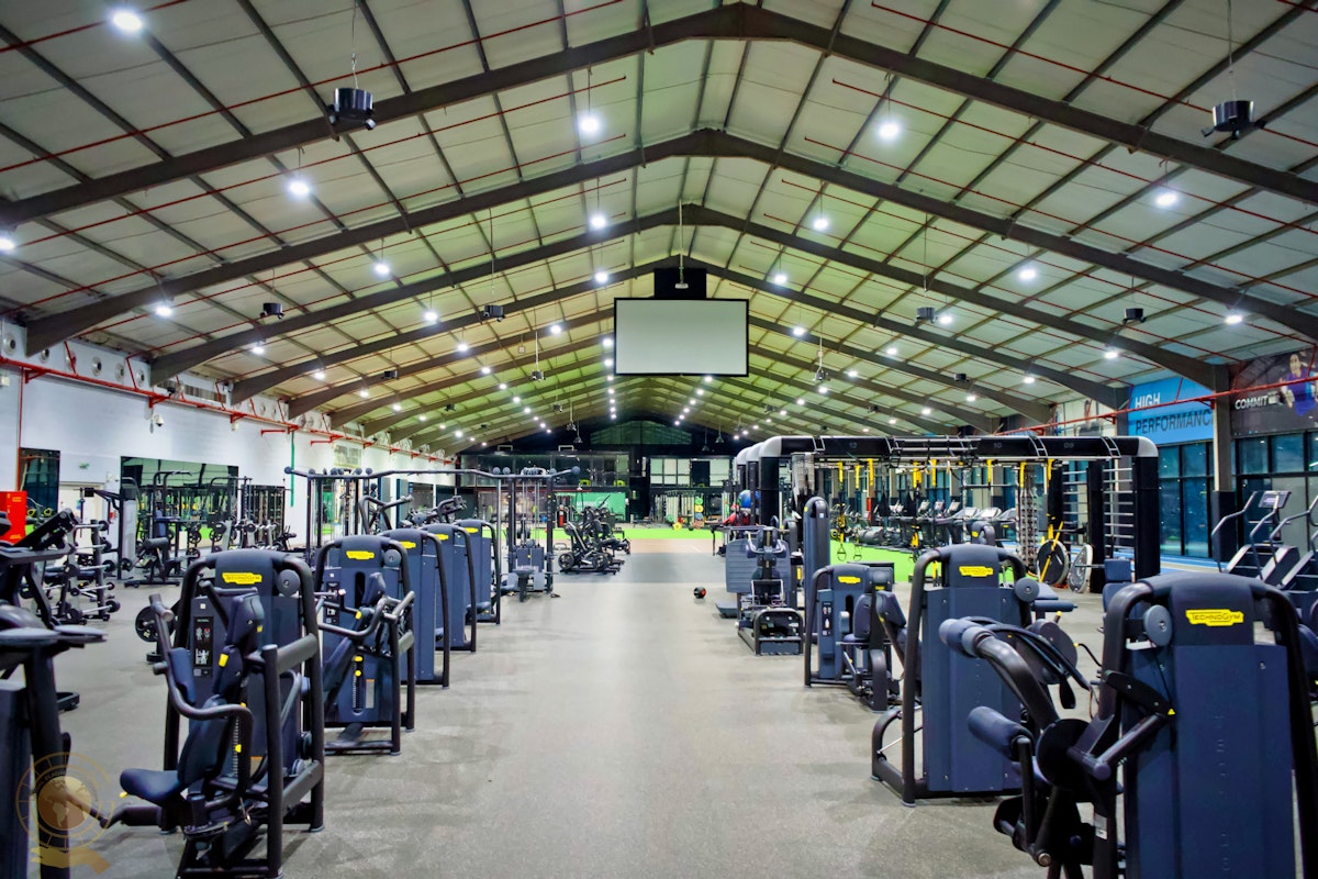 Large fitness center featuring rows of exercise machines, open training areas, and a high ceiling with bright lighting for an airy and well-equipped workout environment.