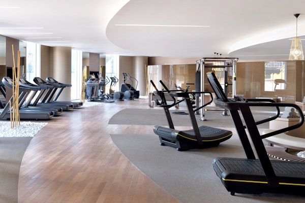 Spacious modern gym with treadmills, ellipticals, and other fitness equipment arranged along a curved wooden floor path