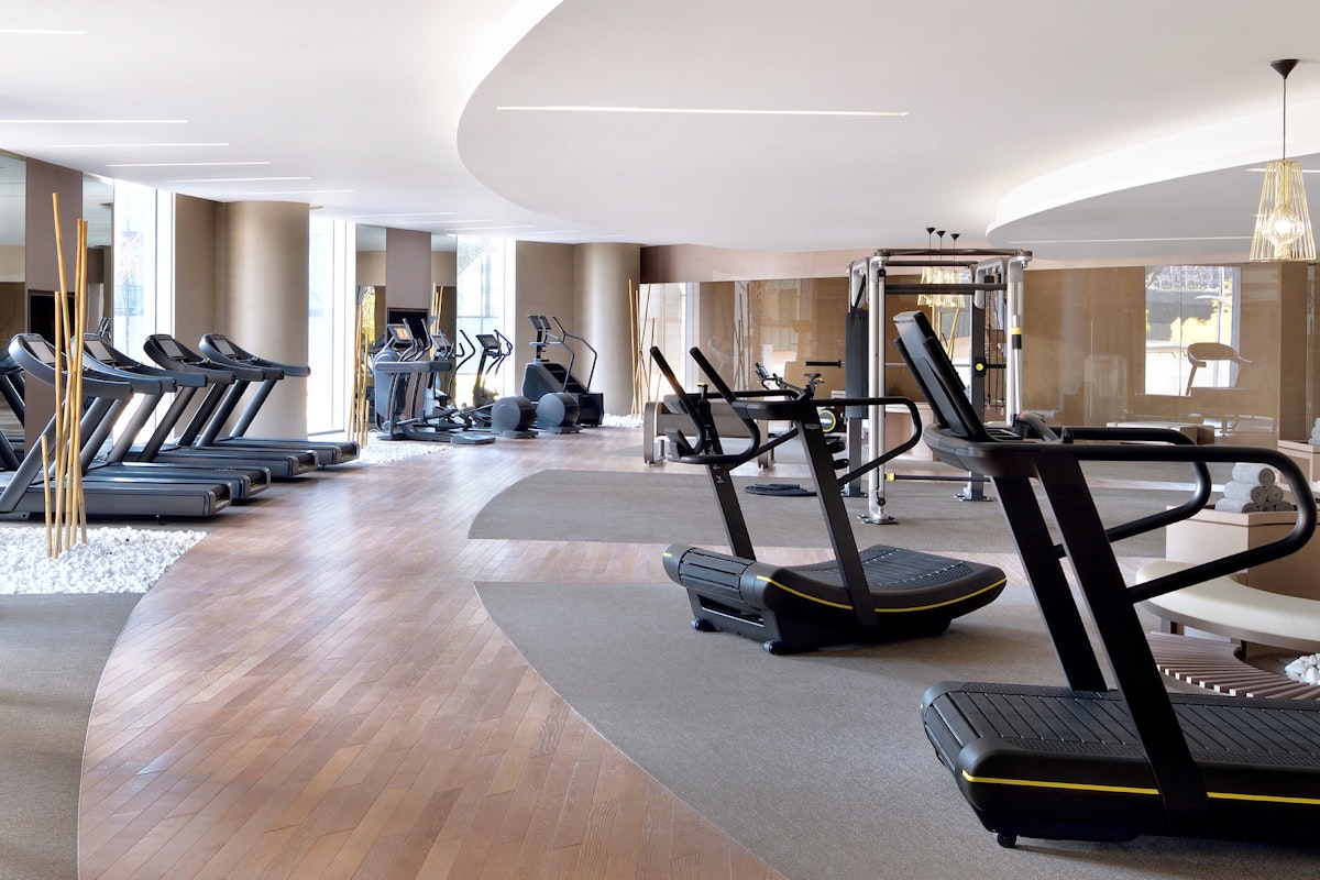 Spacious modern gym with treadmills, ellipticals, and other fitness equipment arranged along a curved wooden floor path