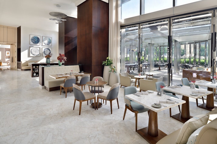 Elegant hotel dining area with modern tables and chairs, large windows allowing natural light, and a view of an outdoor seating area
