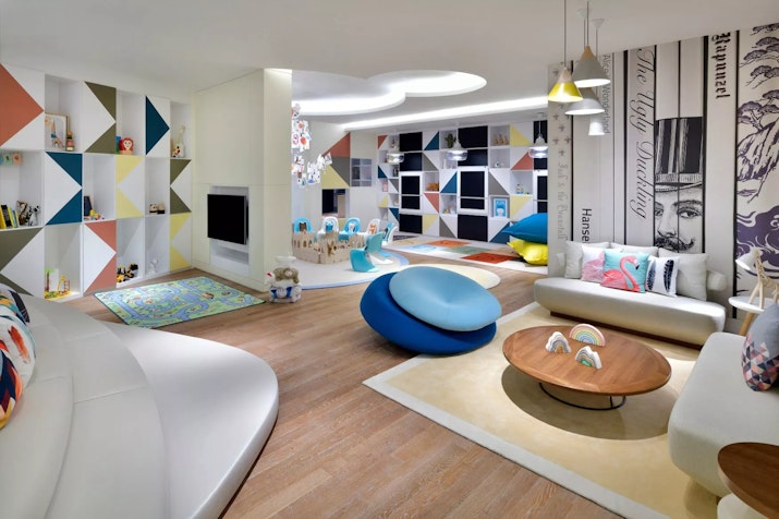Colorful, modern kids' playroom with abstract wall patterns, cozy seating areas, and small play tables and chairs on a wooden floor