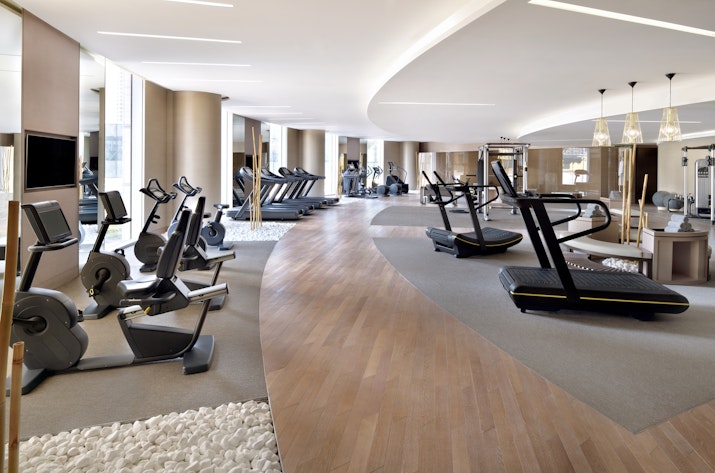 Spacious modern gym with treadmills, ellipticals, and other fitness equipment arranged along a curved wooden floor path