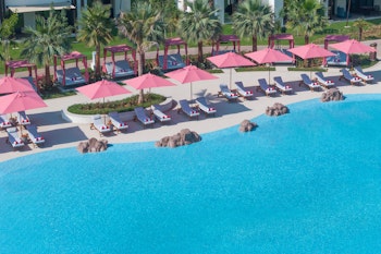 Aerial view of a poolside area with pink umbrellas and lounge chairs surrounded by palm trees.