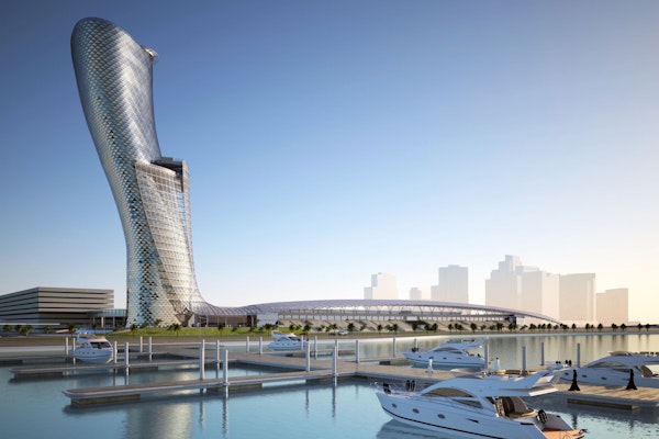 A modern, twisting skyscraper next to a marina with boats, set against a clear sky.