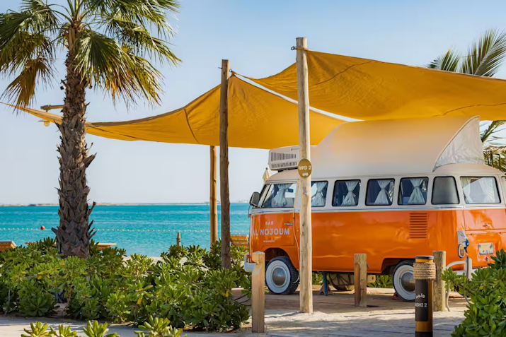 Orange vintage van parked under yellow sunshades by the beach.