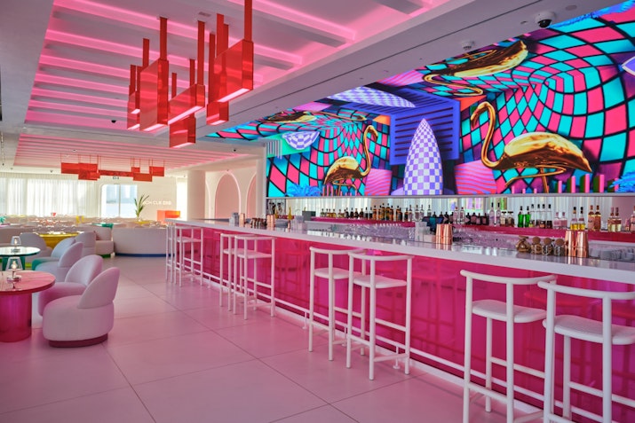 Vibrant bar with pink decor, colorful wall art, and modern seating.