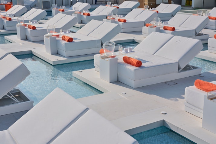 White poolside loungers with orange towels arranged over shallow water.