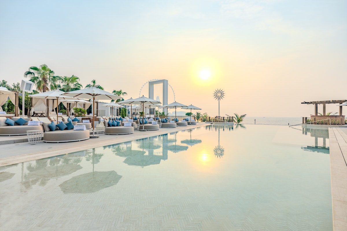 COVEBEACH A serene poolside view at sunset, featuring lounge seating with blue cushions and a clear sky reflecting on the water.