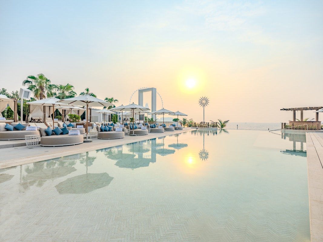 A serene poolside view at sunset, featuring lounge seating with blue cushions and a clear sky reflecting on the water.