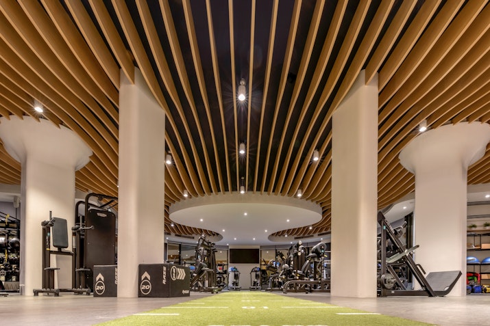 An interior view of a modern gym showcasing a sleek design with wooden slatted ceilings and open space filled with various gym equipment.