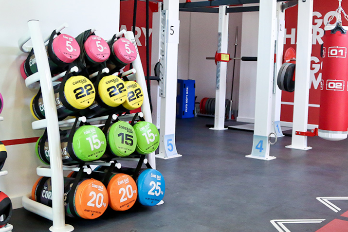 A rack displaying colorful weighted medicine balls in a gym, with various weights labeled, set against a backdrop of gym equipment.