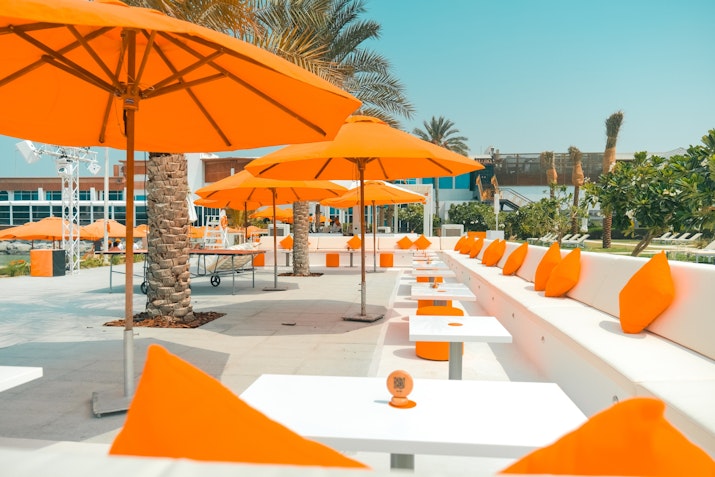 Outdoor seating area with white tables, orange umbrellas, and matching cushions.