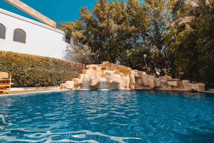 Pool with stone waterfall feature surrounded by lush trees.