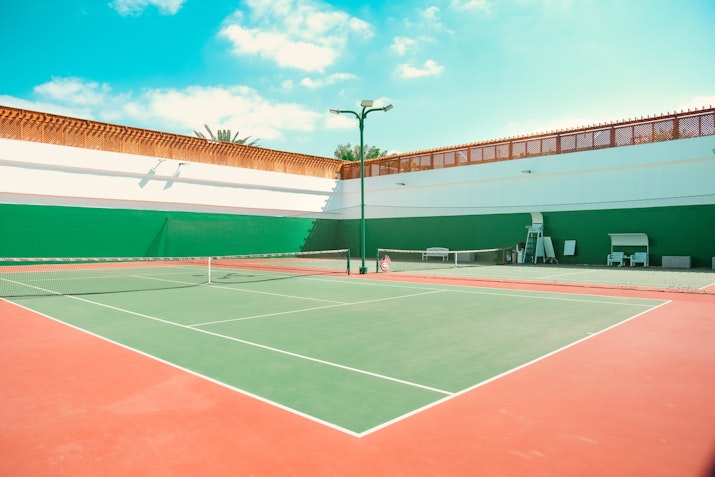 Outdoor tennis court with red and green flooring under a bright sky.