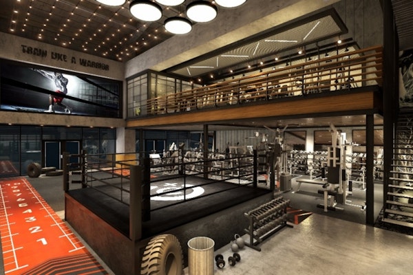 Industrial-style gym interior with high ceilings, showcasing a boxing ring, weightlifting area, and various workout equipment. The space features motivational decor and mezzanine-level seating, creating an intense, focused atmosphere.