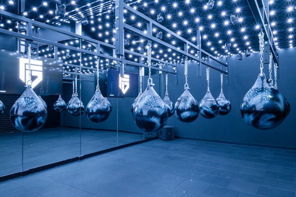 Step into the ring and take your training to the next level with our state-of-the-art boxing setup A modern boxing gym with a row of heavy water-filled boxing bags suspended from the ceiling, illuminated by a grid of small ceiling lights for an ambient, intense atmosphere.