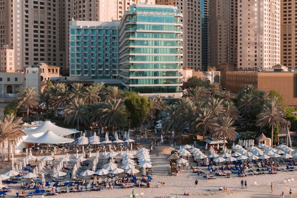Beachfront resort with umbrellas and lounge chairs, surrounded by palm trees and high-rise buildings
