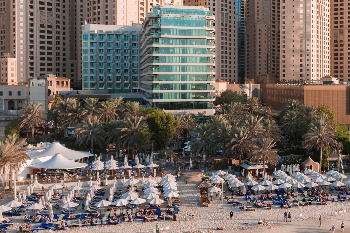 Beachfront resort with umbrellas and lounge chairs, surrounded by palm trees and high-rise buildings