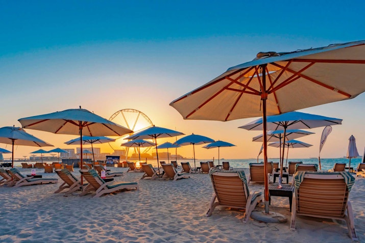 Beach chairs and umbrellas at sunset with a Ferris wheel in the background.