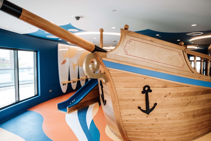 A colorful indoor playground featuring a wooden pirate ship structure with a slide.