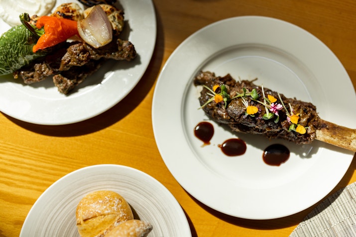 A beautifully presented dish featuring a large piece of meat with garnishes, accompanied by roasted vegetables and a sweet pastry on the side.
