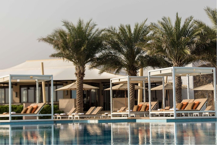 A serene view of a swimming pool surrounded by palm trees and shaded lounge areas with comfortable seating.
