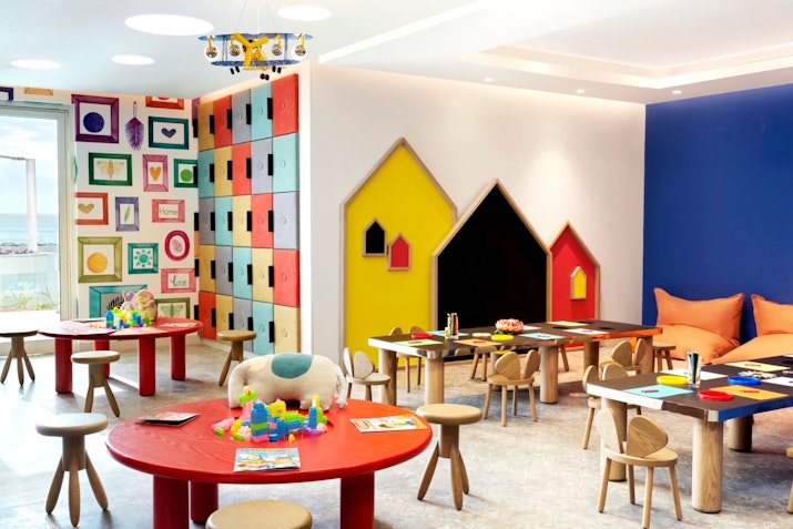 Colorful children's playroom with tables, chairs, and various toys and art supplies.