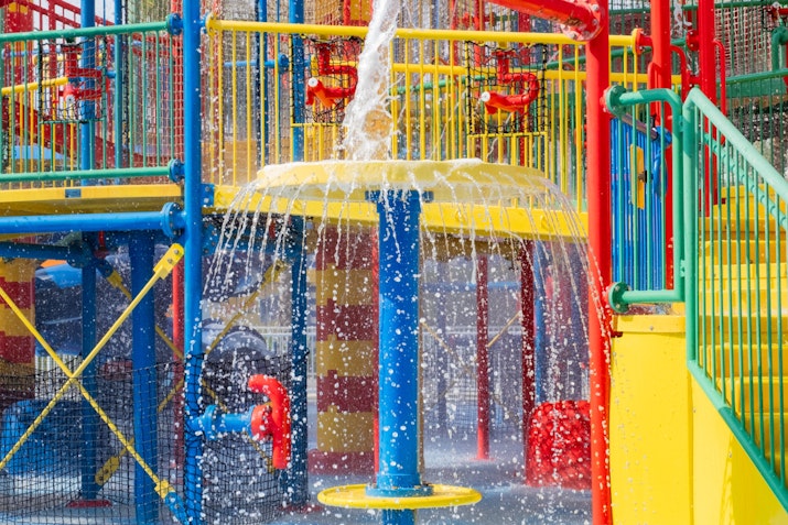 Colorful water play structure with cascading water, featuring yellow, blue, red, and green platforms and railings, creating a vibrant and playful scene at a water park