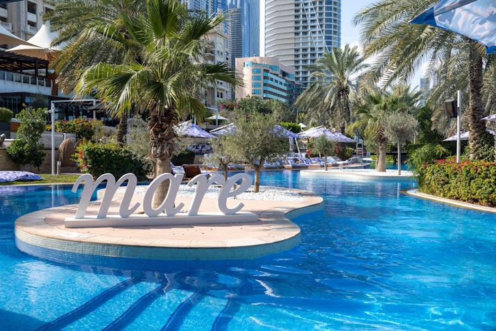 Pool with "mare" sign on an island surrounded by palm trees and lounge chairs.