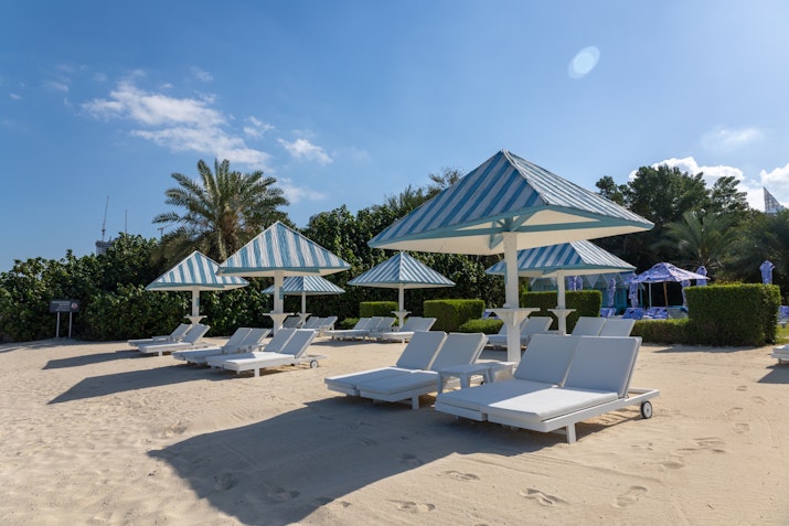 Beach loungers with blue-striped umbrellas on sandy shore.