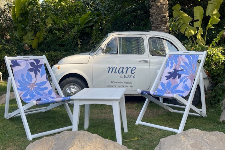 Outdoor seating area with two patterned chairs, a small table, and a vintage car labeled "mare.