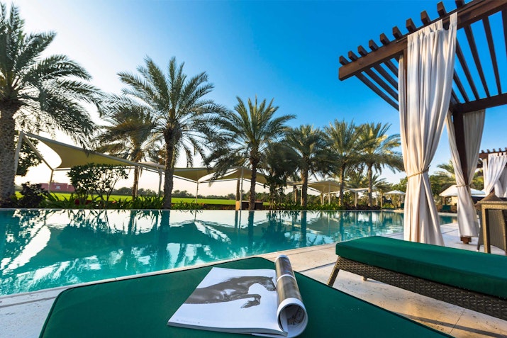 Poolside lounge area with a magazine on a green sunbed and palm trees in the background.