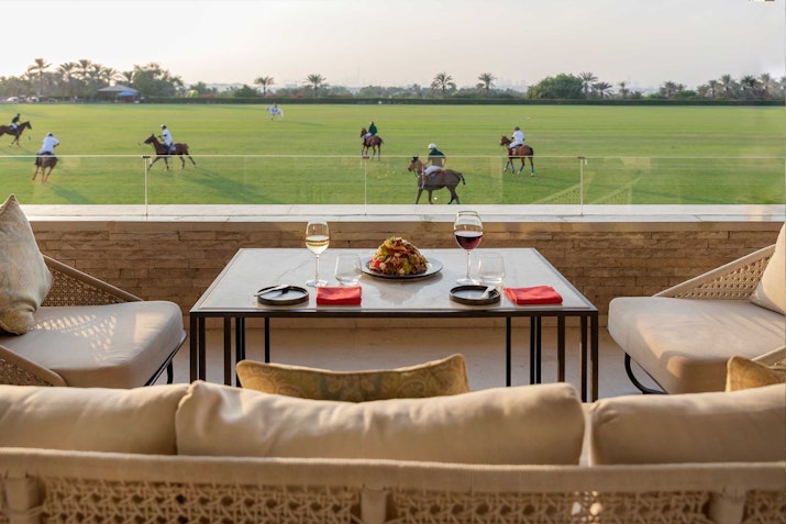 Outdoor seating with a view of a polo field and players.