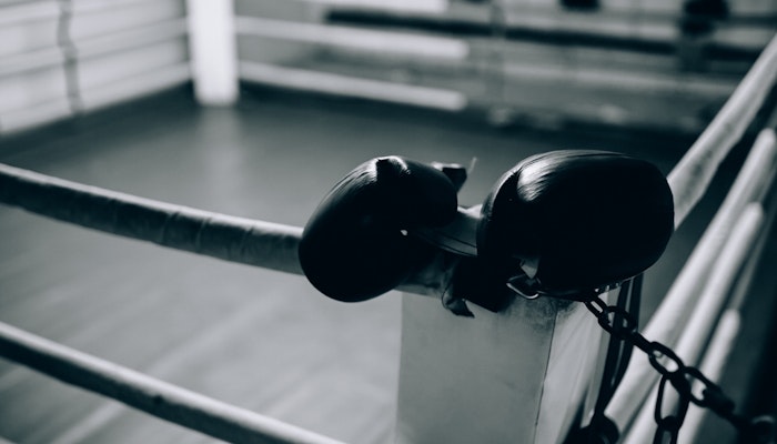 Red Gym with Privilee Boxing gloves draped over the corner post of a vacant boxing ring, evoking a sense of solitude and focus.