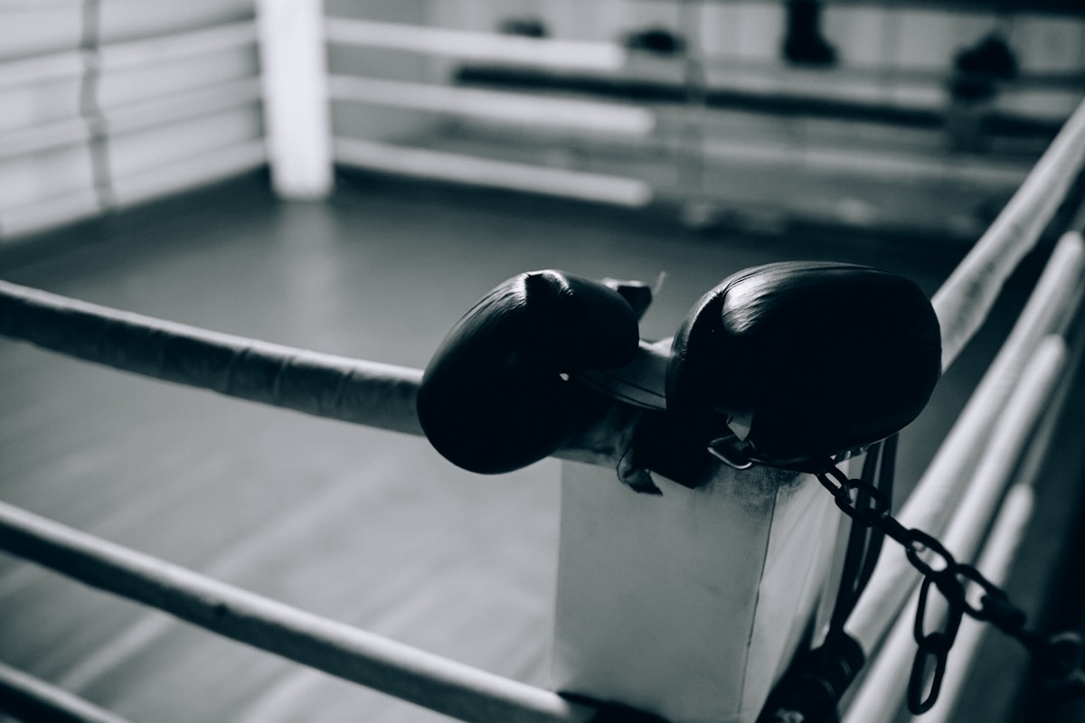 Boxing gloves draped over the corner post of a vacant boxing ring, evoking a sense of solitude and focus.