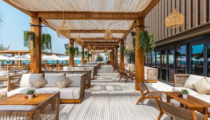 Mövenpick Resort Al Marjan Island A stylish outdoor dining area with wooden furniture, comfortable seating, and lush greenery, creating a relaxed atmosphere by the beach.
