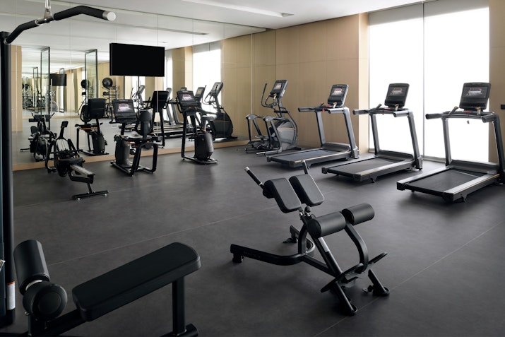 Mövenpick Resort Al Marjan Island Gym A modern gym interior with various exercise equipment, including treadmills and weight machines, and a large mirror reflecting the setup.