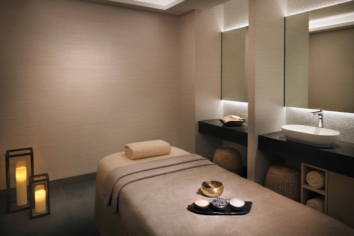 A serene spa treatment room featuring a massage table, ambient lighting with decorative lanterns, and a sink area with organized supplies.