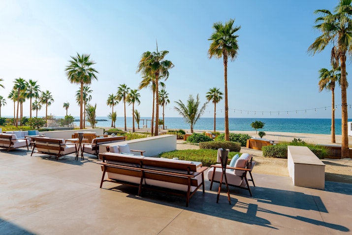Outdoor seating area with wooden benches and ocean view, surrounded by palm trees.