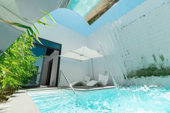 Private pool area with modern loungers and water feature surrounded by greenery.