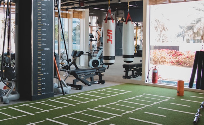 Interior view of a gym with exercise equipment, UFC punching bags, and a turf training area.